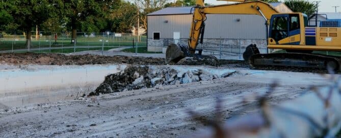 Yellow Excavator Tearing Down Abandoned Public Swimming Pool