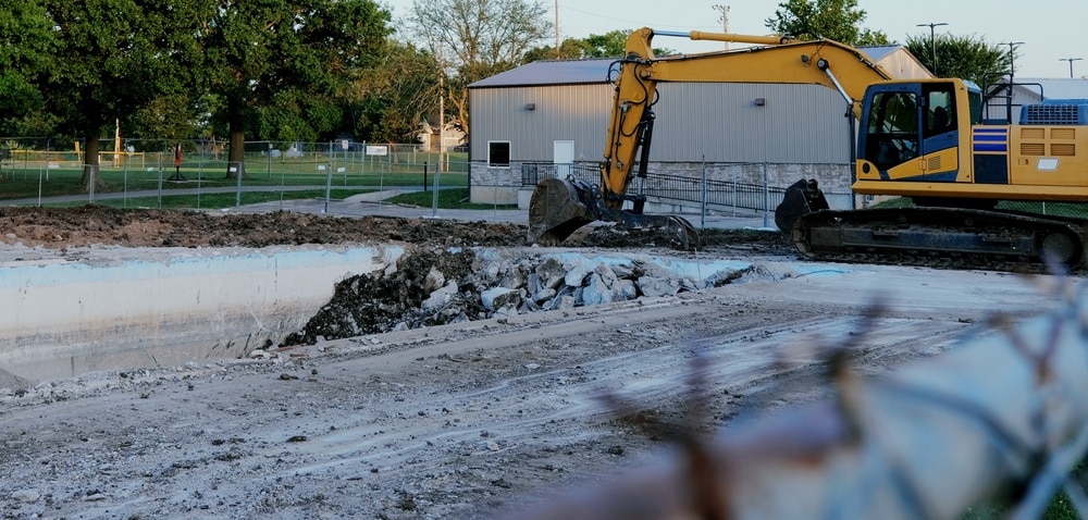 Yellow Excavator Tearing Down Abandoned Public Swimming Pool